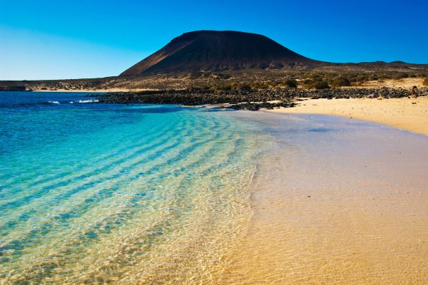 Crystal clear water at beach of La Francesa with the volcano Montana Amarilla in background.